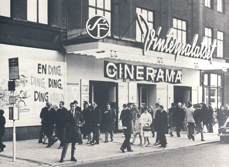 This black and white photograph depicts movie-goers on the sidewalk outside a Cinerama theater. The Cinerama logo is plainly visible on the front of the building above the multiple entrances.