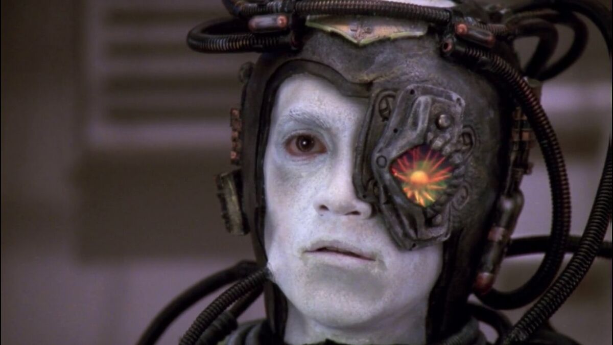 A humanoid Borg with characteristic chalky skin and robotic eyepiece confers with the Collective.
