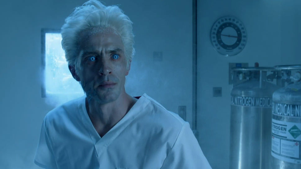 Seen in an antiseptic room with a cold, bluish tint, Mr Freeze appears center-frame with white hair, unnaturally light blue glowing eyes, and what looks like a white hospital gown.