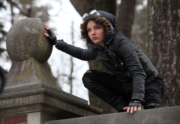 Selina Cat Kyle from Gotham perches upon a gothic building, in a catlike stance. She is wearing dark clothing with a fur-lined hood.