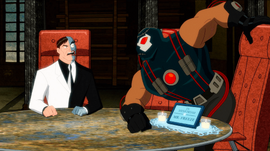 Two-Face, a scarred man in a dress suit, sits at an executive chair while Bane, a large muscular man in a costume, tries to sit in another executive chair that is labelled "In memoriam of Mr. Freeze"