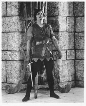 Fairbanks Robin Hood standing by wall w sword
