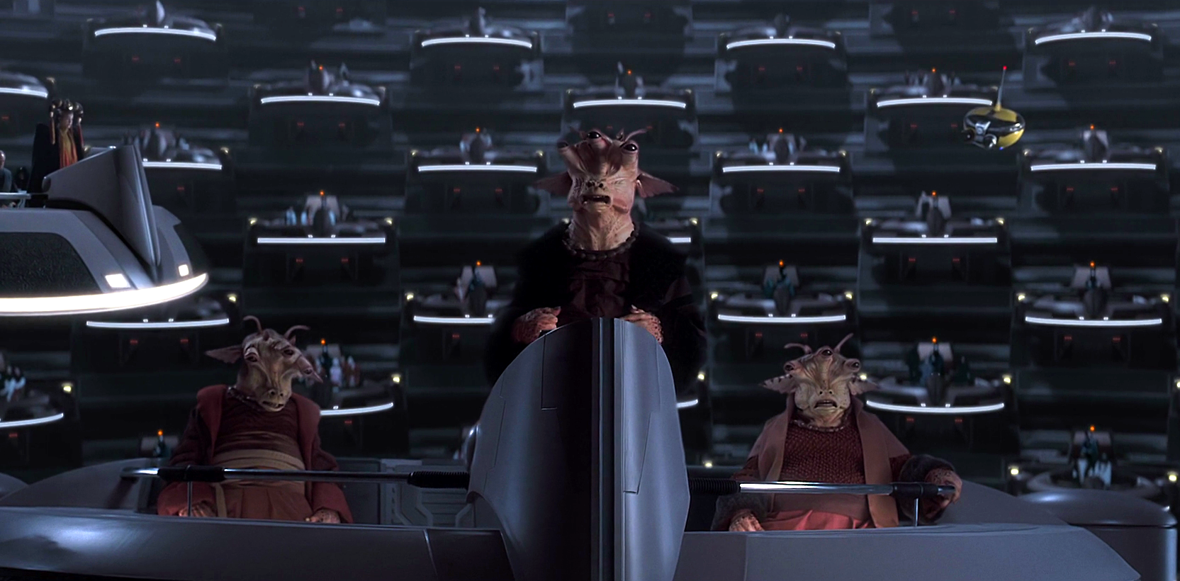 Em primeiro plano, vemos três alienígenas de três olhos da raça Gran. Eles estão em uma plataforma flutuante do Senado Galáctico, com trajes de gala. O alienígena do meio está de pé.